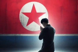 Pessoa ajoelhada orando com a bandeira da Coreia do Norte ao fundo